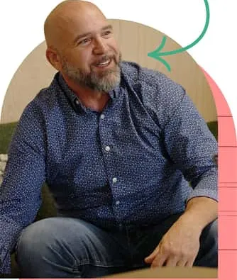 Smiling bearded man in navy patterned shirt sits framed by arrow