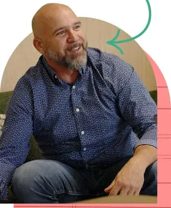 Smiling bearded man in navy patterned shirt sits framed by arrow