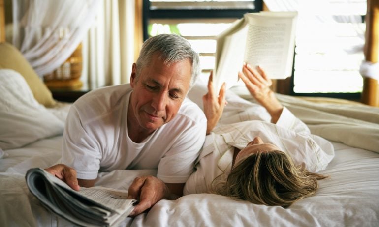 A couple reading and relaxing on a bed — an abstract representation of the financial security that can come from choosing the best investments