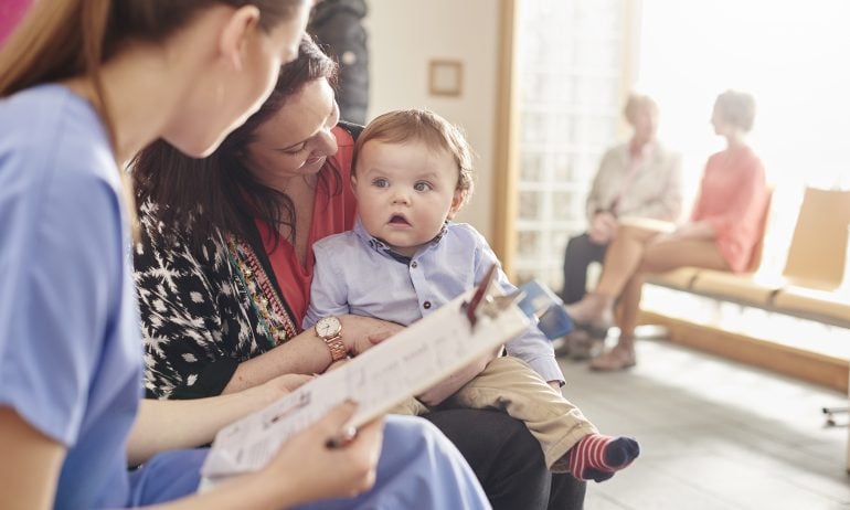 Mom holds a baby boy as they talk with a nurse at a doctor's office