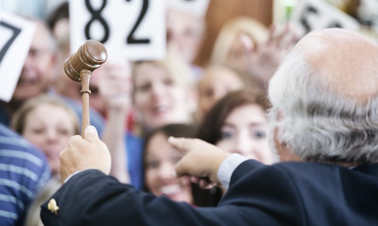 An auctioneer with a gavel points to bidders