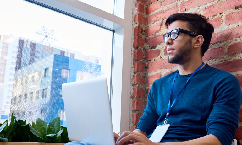 Young man with laptop looking out window