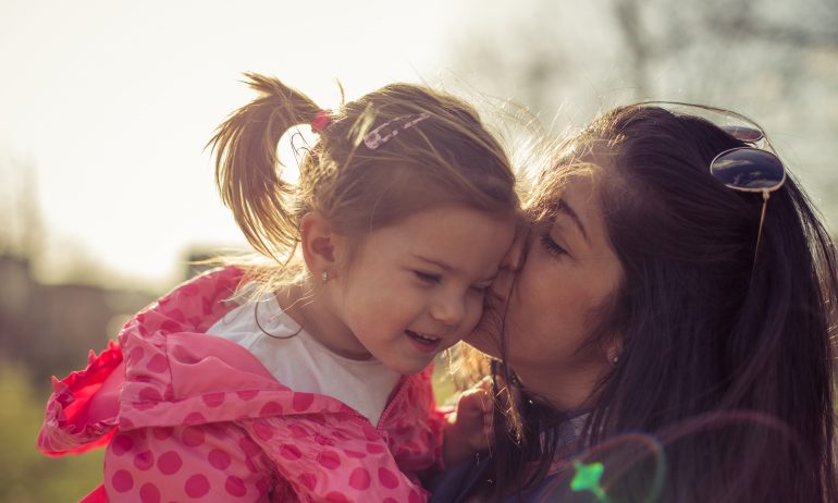 A mom kisses her toddler daughter