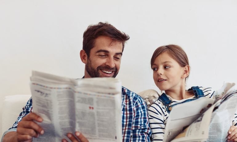 A father and child looking at a newspaper together — an abstract representation of financial education, such as learning how to invest in the S&P 500.