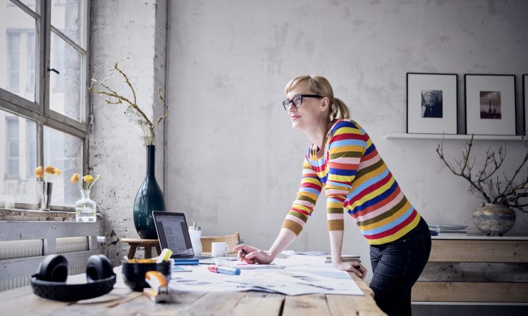 Portrait of smiling woman standing at desk in a loft looking through window