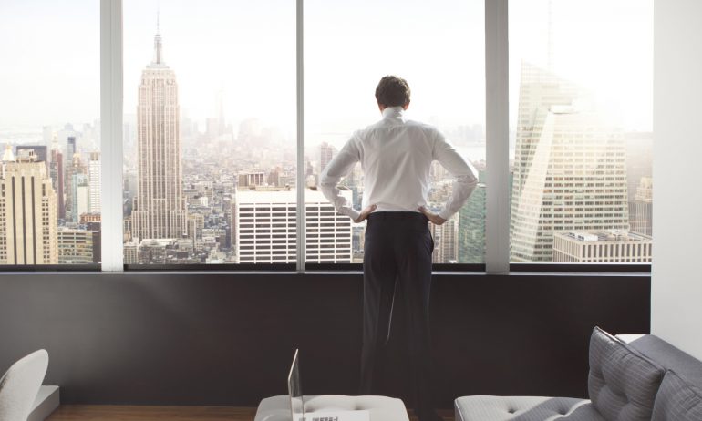 Man looking through window at cityscape stock photo - OFFSET