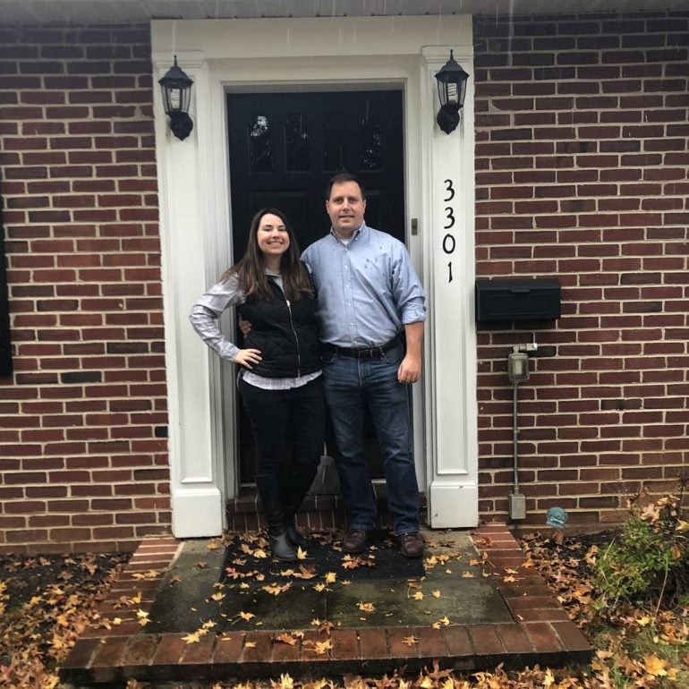 Kristen and Robert Toth Jr. standing in the doorway of their brick ranch house built in the 1950s.