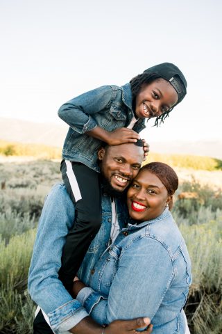 Image of Sylvester Akpan holding son Aiden on his shoulders and wife Karen Akpan standing next to them outside.