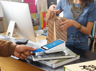 A customer inserts his credit card into the Square Terminal while the cashier holds a paper bag for him.