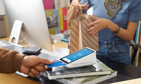 A customer inserts his credit card into the Square Terminal while the cashier holds a paper bag for him.