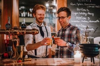 Two men toast behind a bar.