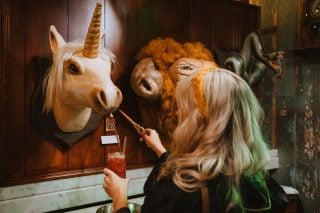 A woman uses a wand to activate a drink station that looks like a unicorn head to refill her glass.