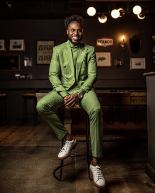 Ramon Smothers sits on a stool wearing a green pinstriped suit.