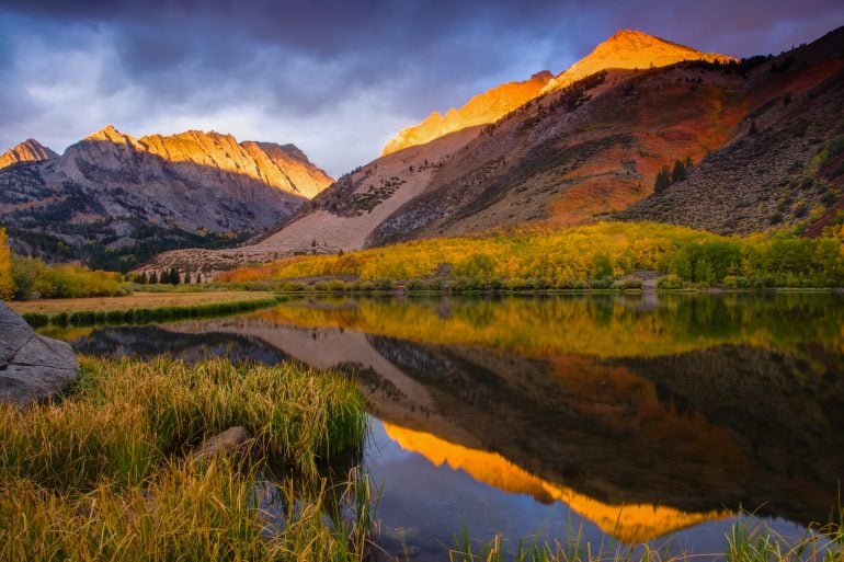 Thin lines of sunlight, a combination of the surrounding geography and the cloud patterns, form on the tips of the foothills of the Sierra Nevada at North Lake, during a vibrant fall foliage season in 2010.