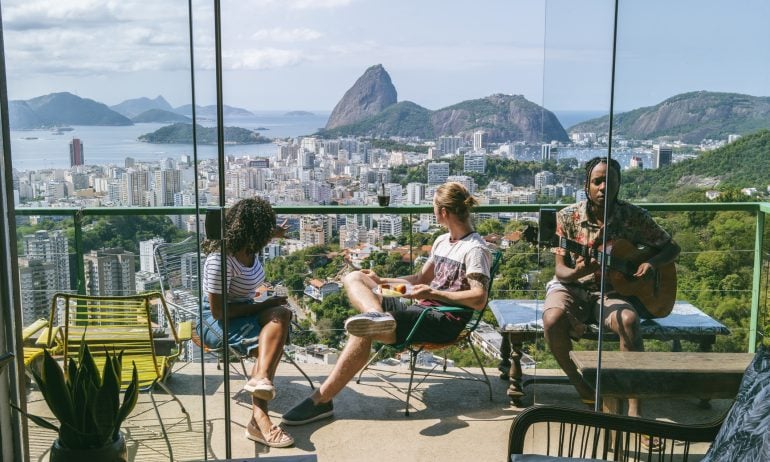 Elevated view of Rio de Janeiro cityscape, man playing guitar with two friends relaxing and listening in sunlight