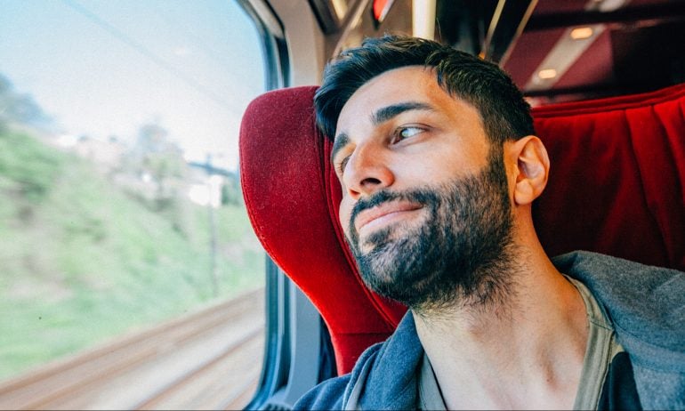 Happy young man is traveling first class on a train sitting and smiling looking out through the window