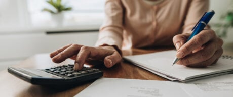 Close up of unrecognizable woman using calculator while going through bills and home finances.