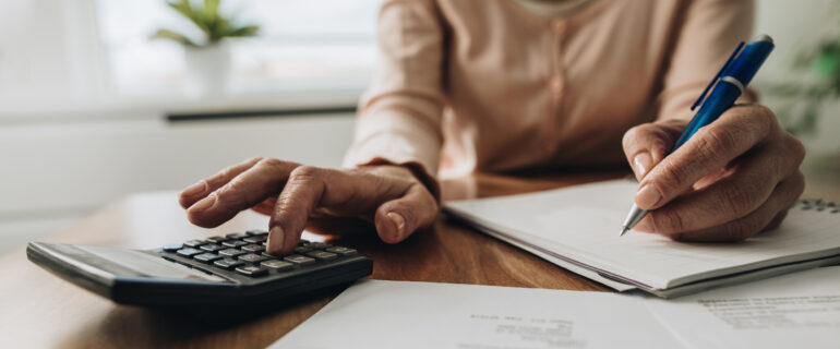Close up of unrecognizable woman using calculator while going through bills and home finances.