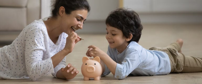 Mother teaching son about saving money and putting coins in piggybank.