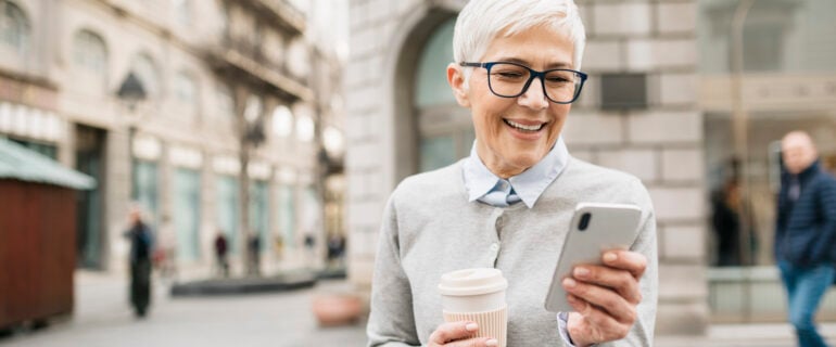 Senior businesswoman checks her no-fee bank account in the middle of the city using her smart phone.