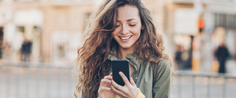 Girl checks her online bank account using her mobile phone while walking down the street.