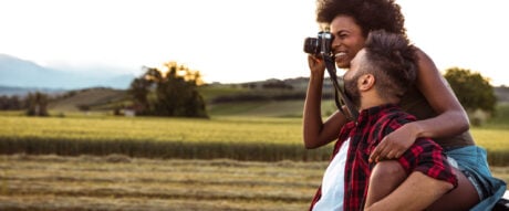 A credit card annual fee pays for premium perks, like vacation travel, roadside assistance, lounge visits and experiences enjoyed by the pictured couple, taking photographs and having fun on a roadtrip.