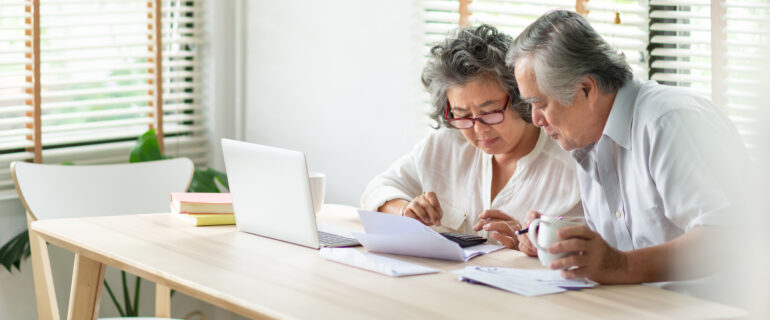A senior Asian couple considers ways to get out of debt while sitting at their kitchen table.