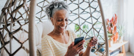 Senior woman using her credit card points while sitting in a wicker chair.