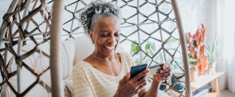 Senior woman using her credit card points while sitting in a wicker chair.