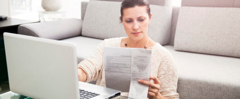 Woman files her income taxes using a laptop in her living room.