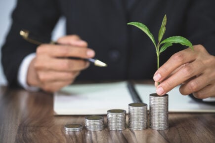 Hand on desk with growing piles of money thanks to smart investing.