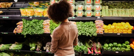 Woman standing in produce section thinking about how to save money on groceries.