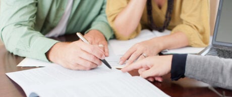 A couple signs papers while getting a loan from the bank.