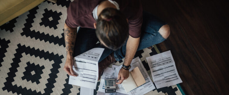 Young man surrounded by papers, making a plan to deal with his debt.