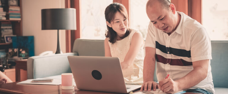 Asian couple writing a will with a laptop on their coffee table.