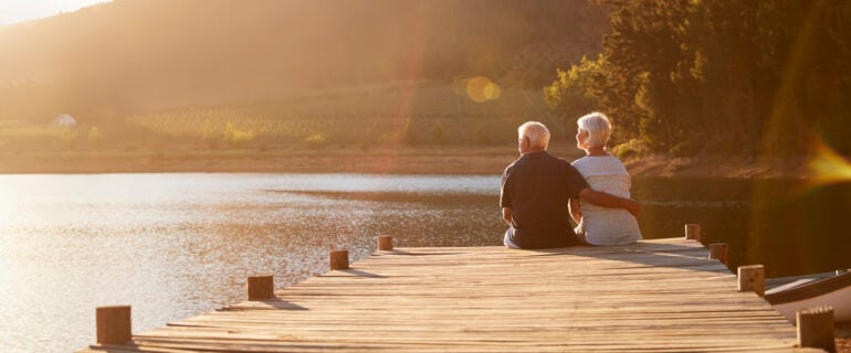 Senior couple sits by lake, enjoying their retirement.