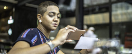 Young woman in the cafe depositing check by phone into an online savings account.