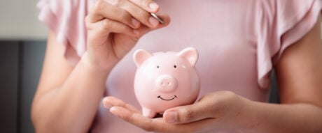 Close-Up Woman Hand is Putting a Money Coin into Piggy Bank on The Bedroom., Female Hand is Inserting Coin in Pink Piggy Saving.