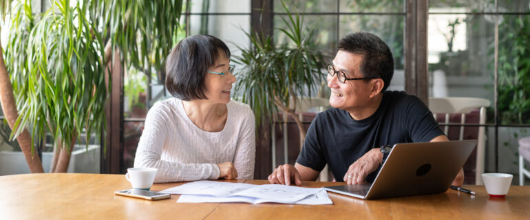 Asian couple talking about their retirement plans in a room filled with light and plants.