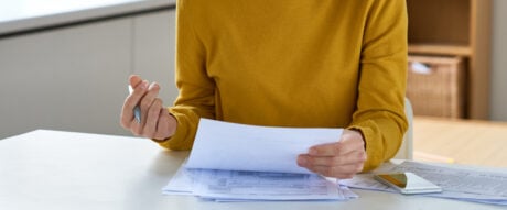 Serious concentrated young woman in glasses sitting at table and analyzing tax documents in home office