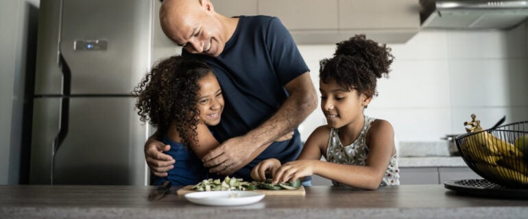 Father embracing daughter while cooking at home