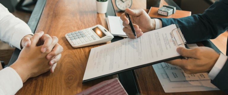 Two people are sitting at a desk with mortgage documents.