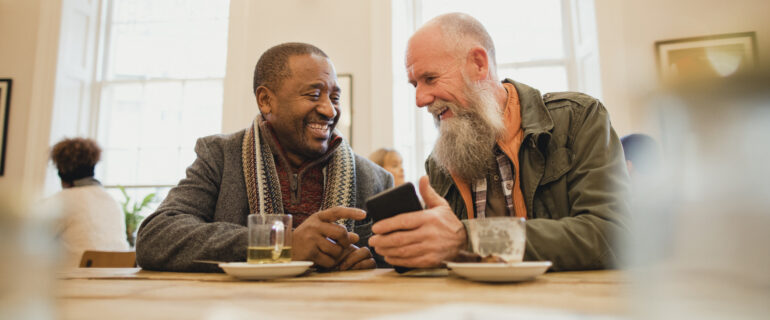 Two men discuss GICs vs mutual funds while drinking coffee in a cafe.