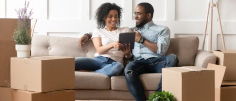 Smiling black couple discusses land transfer tax rates while sitting on couch.