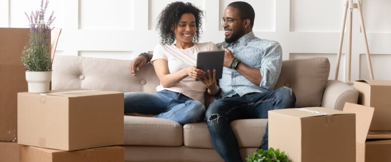 Smiling black couple discusses land transfer tax rates while sitting on couch.