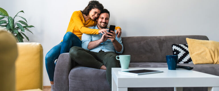 Cheerful couple on couch researching home insurance.