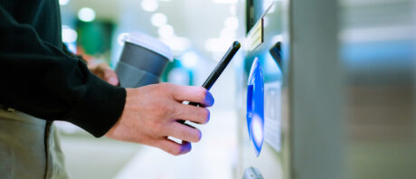 A person makes a contactless payment using a smart phone at a kiosk.