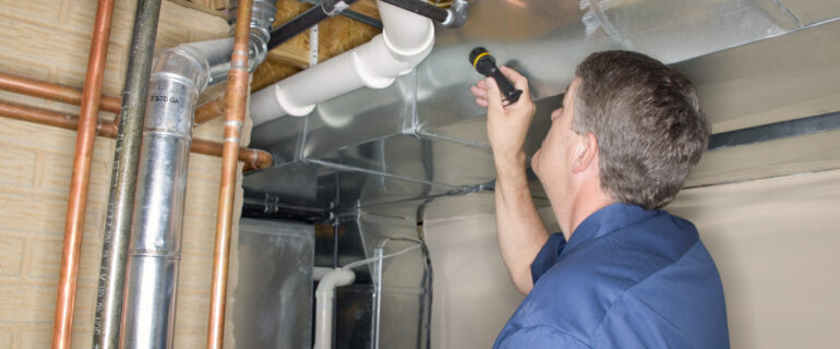 Man with a flash light evaluates basement plumbing during a home inspection.