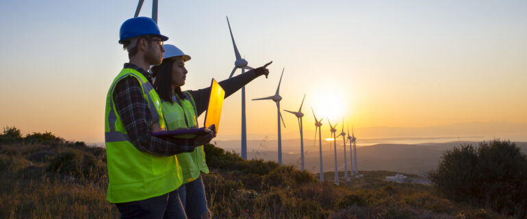 Two wind turbine engineers discuss the benefits of ESG investing while the sun sets in the distance.