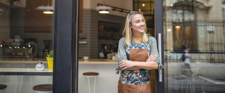 Young cafe owner who is financially independent standing in front of her business.